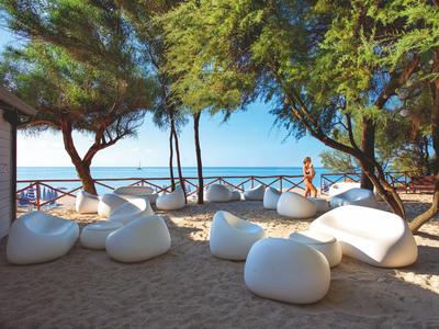 Outdoor-Lounge mit weißen Sitzsäcken unter Bäumen am Strand mit Meerblick.