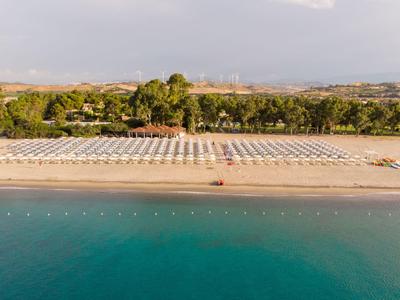 Leerer Strand mit Sonnenschirmen und ruhigem Meer vor einer Palmengesäumten Küste