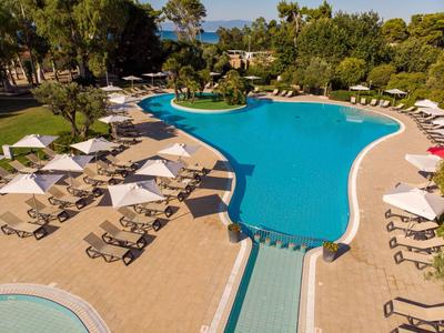 Großer, klarer Pool mit Sonnenliegen und weißen Schirmen, umgeben von grünen Bäumen und Sträuchern.