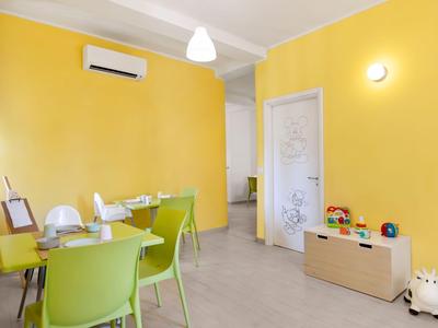 Moderner Hotelaufenthaltsraum mit gelben Wänden, grünem Tisch und Stühlen sowie Spielzeug für Kinder.