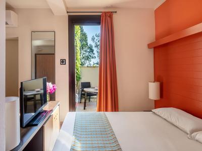 Ein helles Hotelzimmer mit Doppelbett, orangefarbener Wand und Blick auf einen Balkon.