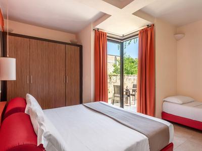 Hell eingerichtetes Hotelzimmer mit Doppel- und Einzelbett und Zugang zum Balkon.