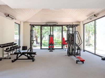 Helle, moderne Fitnesseinrichtung mit Geräten und Hanteln, großen Fenstern und Blick ins Grüne.