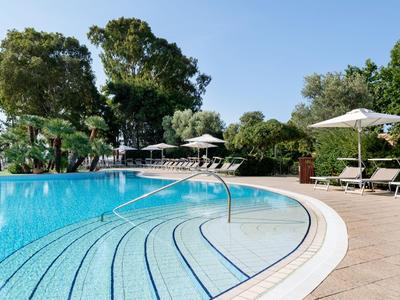 Großer Pool mit Treppen und Sonnenliegen in einer grünen, sonnigen Umgebung