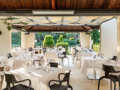 Hell eingerichtetes Restaurant mit weißen Tischtüchern, schwarzen Stühlen und Blick auf einen Garten.