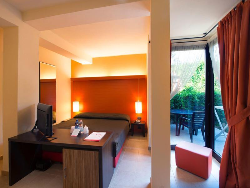 Modernes Hotelzimmer mit Doppelbett, Schreibtisch, Fernseher und Balkon mit Gartenausblick.