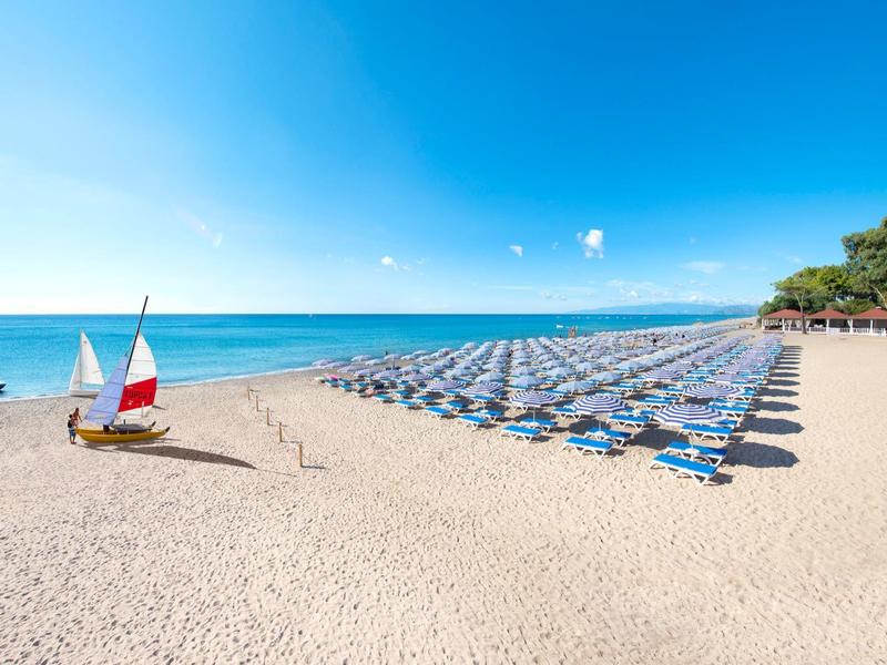 Leerer Sandstrand mit Reihen von Liegestühlen und einem kleinen Boot am Wasser.