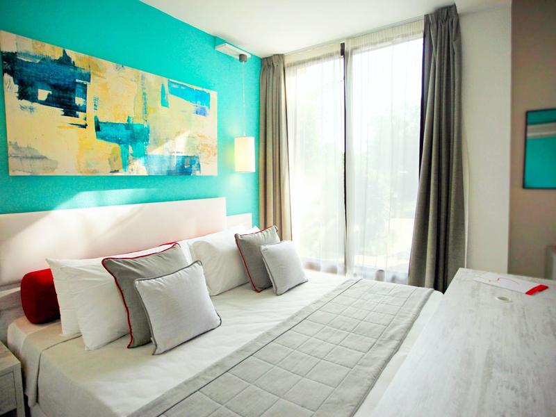 Helles Schlafzimmer mit großem Bett, türkisfarbener Wand, abstraktem Gemälde und bodentiefen Fenstern.