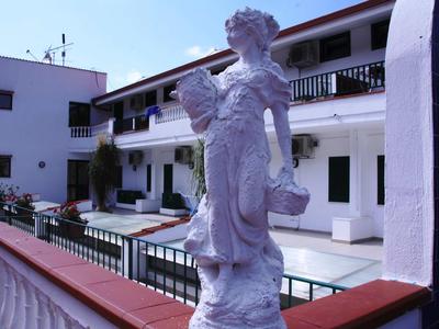 Weiße Statue einer Frau in einem Innenhof eines Hotels mit weißen Gebäuden im Hintergrund.