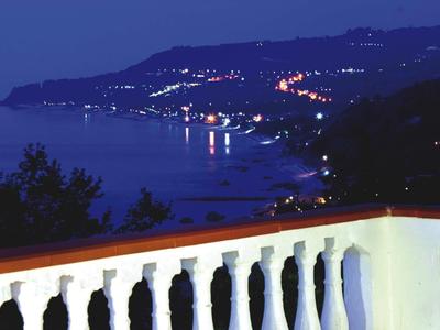 Widok z balkonu nocą na nadmorskie miasto z światłami i wzgórzami.
