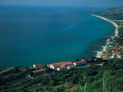 Küstenlinie mit blauem Meer, Häusern und grünen Hügeln unter klarem Himmel.