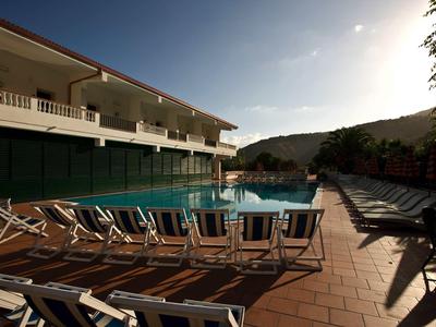Hotelpool mit Liegestühlen auf einer Terrasse bei Sonnenuntergang und Hügeln im Hintergrund