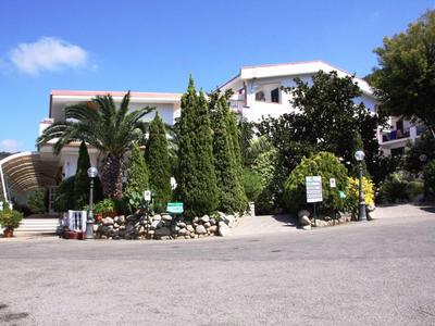 Wejście do hotelu z palmami i zielenią pod niebieskim niebem.