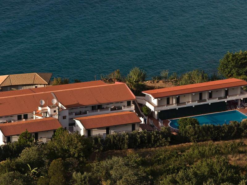 Kompleks hotelowy z czerwonymi dachami i basenem blisko wybrzeża z widokiem na morze