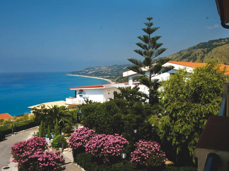 Widok na morze i ogród z kwitnącymi krzewami obok budynku hotelu.