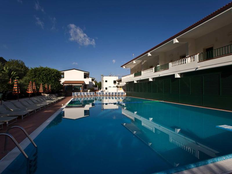 Basen hotelowy z leżakami pod czystym niebem, nowoczesny dwupiętrowy budynek w tle.