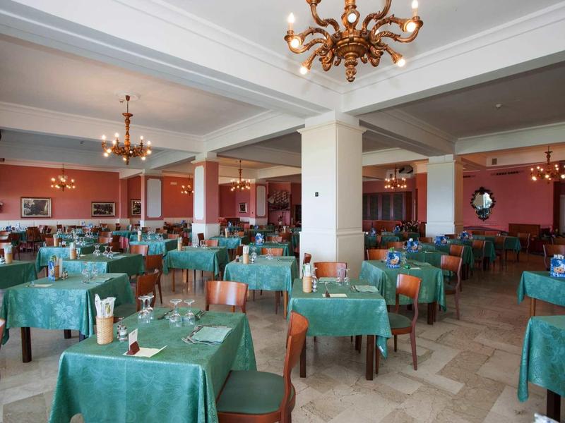 Duża jadalnia z zielonymi nakryciami stołów i złotymi żyrandolami.