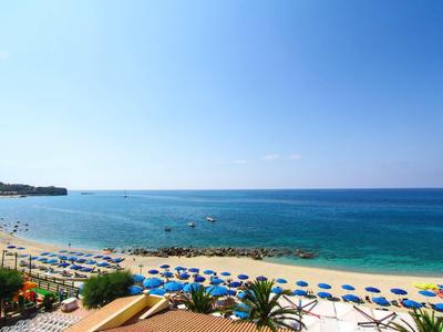 Strand mit blauem Meer, klarem Himmel, Sonnenschirmen und Liegestühlen in Reihe am Sandufer.