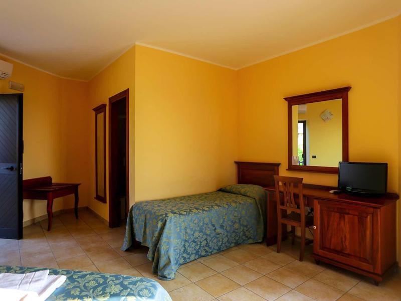 Zimmer mit gelben Wänden, grünem Bett, Holzmöbeln und kleinem Fernseher auf Kommode.