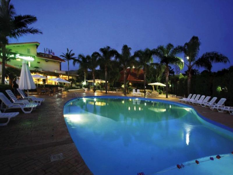 Piscine d'hôtel la nuit avec chaises longues et palmiers.