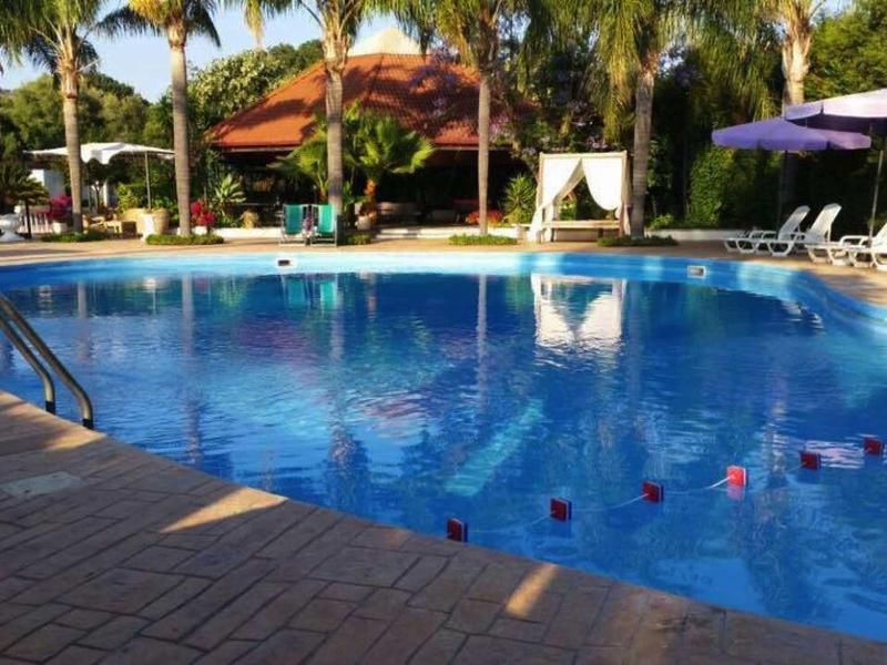 Piscine ronde d'hôtel avec chaises longues et palmiers en arrière-plan par temps ensoleillé.