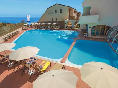 Großer Außenpool mit Liegestühlen und Sonnenschirmen neben einem weißen Gebäude mit Meerblick.