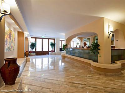 Große helle Lobby mit Marmorfußboden, Pflanzen, Wandbildern und geschwungenem Empfangstresen.