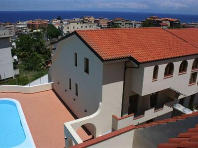 Haus mit rotem Ziegeldach, blauem Pool und Blick auf das blaue Meer im Hintergrund.