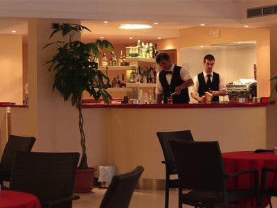 Innenraum eines Restaurants mit zwei Kellnern hinter der Theke und mehreren Tischen mit roten Tischdecken.