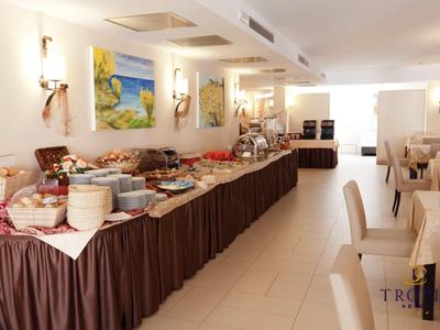 Buffet mit verschiedenen Speisen in hellem, modernem Frühstücksraum mit beigen Wänden und Stühlen.