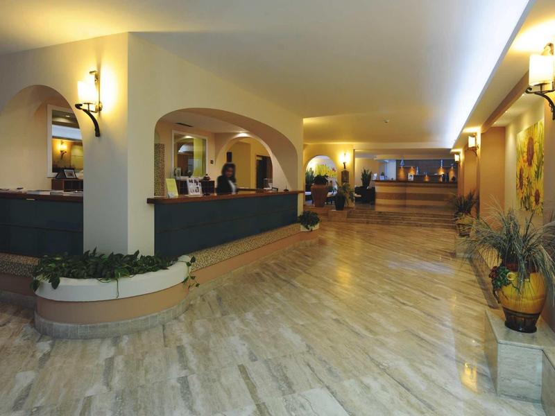 Weite Hotellobby mit Marmorboden, Empfangstresen und floraler Dekoration im warmen Licht.