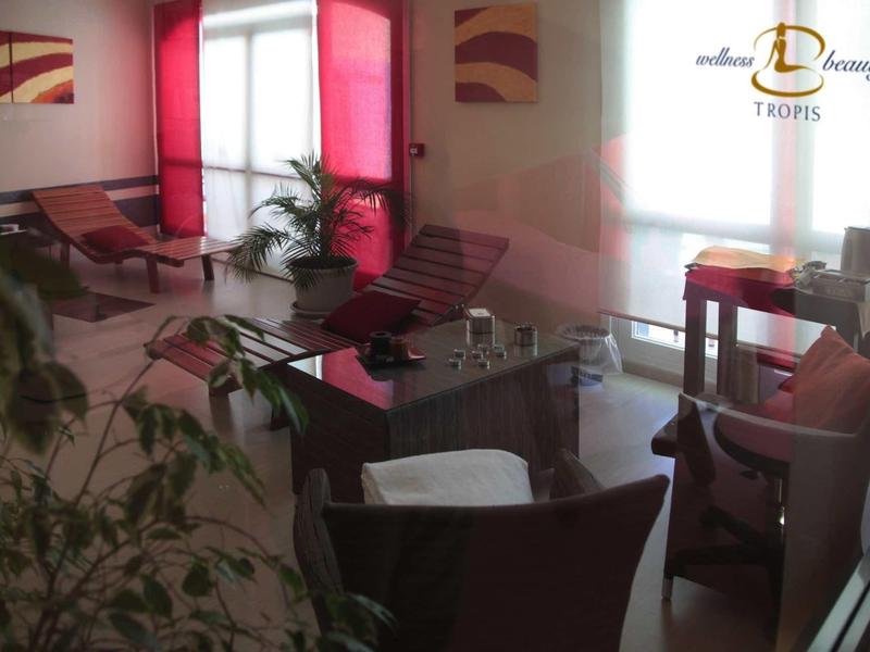 Heller Warteraum mit roten Akzenten, Pflanzen, Sesseln und Tischen, ruhig und einladend gestaltet.