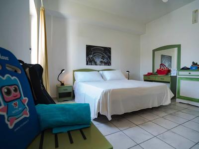 Bright hotel room with double bed, green-white dresser, and blue cushions.