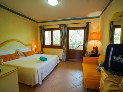 Bright hotel room with double bed, orange furniture, and view outside through window and door.