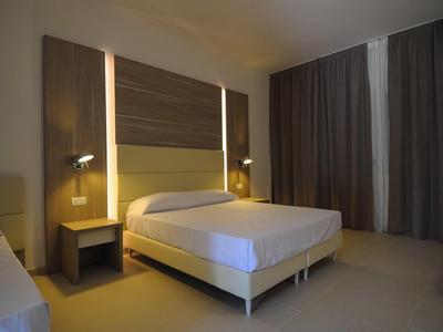 Modern hotel room with double bed, wooden wall panel, and subdued lighting.