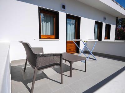 White terrace with two chairs and a drying rack in front of building windows.