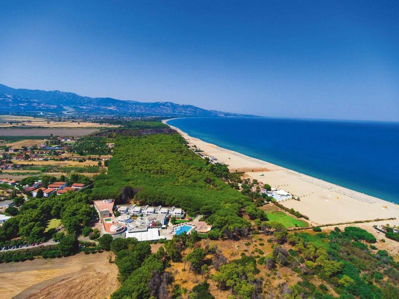 Aerial view of a hotel by the long sandy beach with blue sea and forested coastline.
