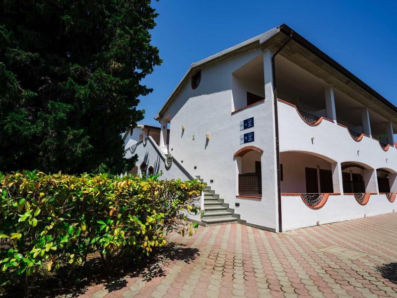 Bright white building with brown shutters and stairs under clear blue sky.