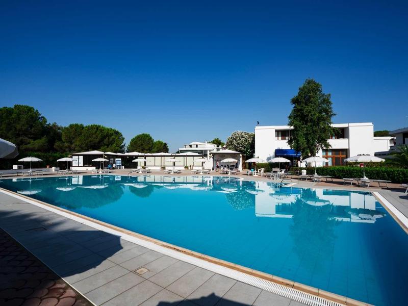 Modern pool area with lounge chairs and umbrellas in front of a white hotel building under clear sky.