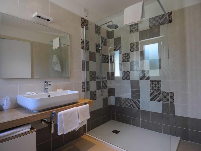 Modern bathroom with large shower, decorative tiles, and sink with towel.