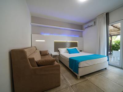 Camera d'hotel moderna con letto matrimoniale, poltrona marrone e accesso alla terrazza.