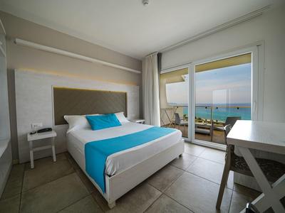 Camera d'hotel moderna con letto matrimoniale, accenti blu e vista mare tramite porta scorrevole in vetro.