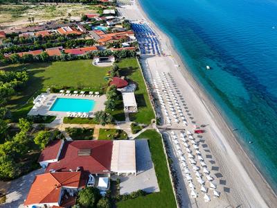 Vista aerea di un hotel con piscina accanto a una lunga spiaggia sabbiosa e mare blu chiaro.