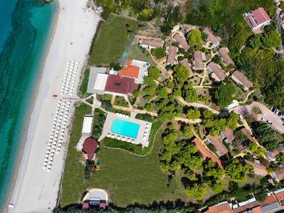Luftaufnahme eines Resorts mit Pool, Strand und mehreren Gebäuden in grüner Umgebung.