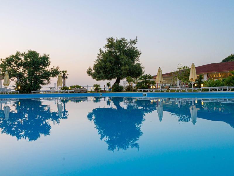 Piscina tranquilla con alberi e lettini al tramonto.