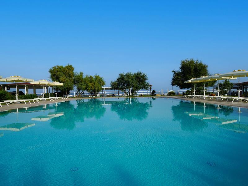 Grande piscina con lettini e ombrelloni sotto un cielo azzurro limpido.
