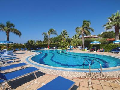 Piscine extérieure ronde avec chaises longues bleues et palmiers sous un ciel clair.