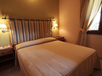 Chambre d'hôtel confortable avec grand lit double, tables de nuit, éclairage chaud et fenêtre avec rideaux.