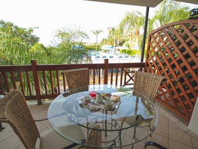 Balcon avec table en verre et quatre chaises donnant sur des palmiers et de l'eau