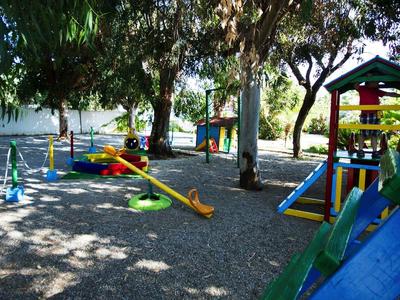 Aire de jeux ensoleillée avec structures d'escalade et balançoires sous les arbres dans le jardin de l'hôtel.